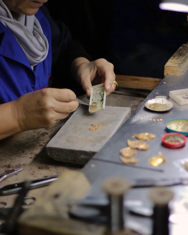 Manos de artesano trabajando una pieza de joyería con herramienta fina sobre el banco de un taller