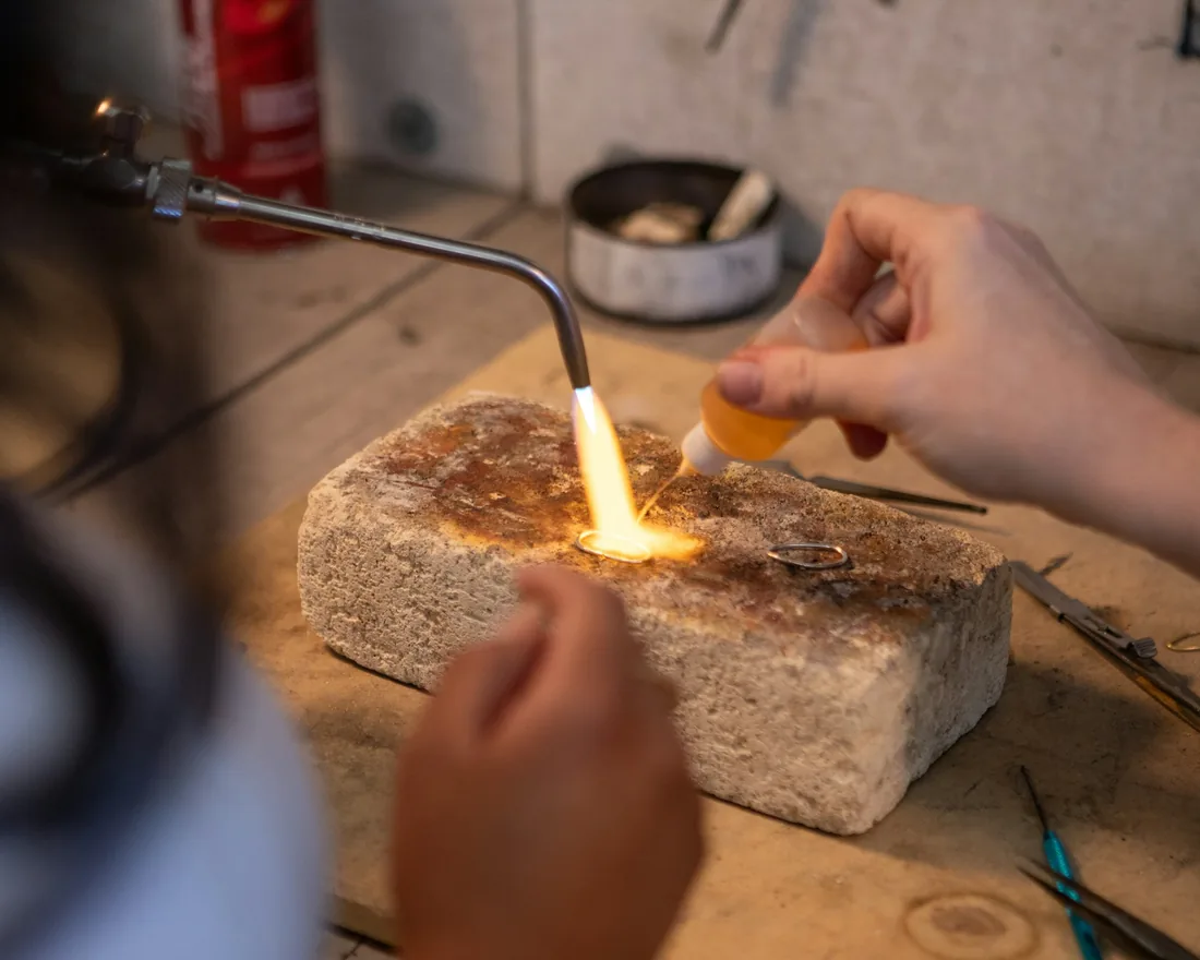 Banco de joyería con soplete encendido calentando una pieza de metal entre herramientas de taller